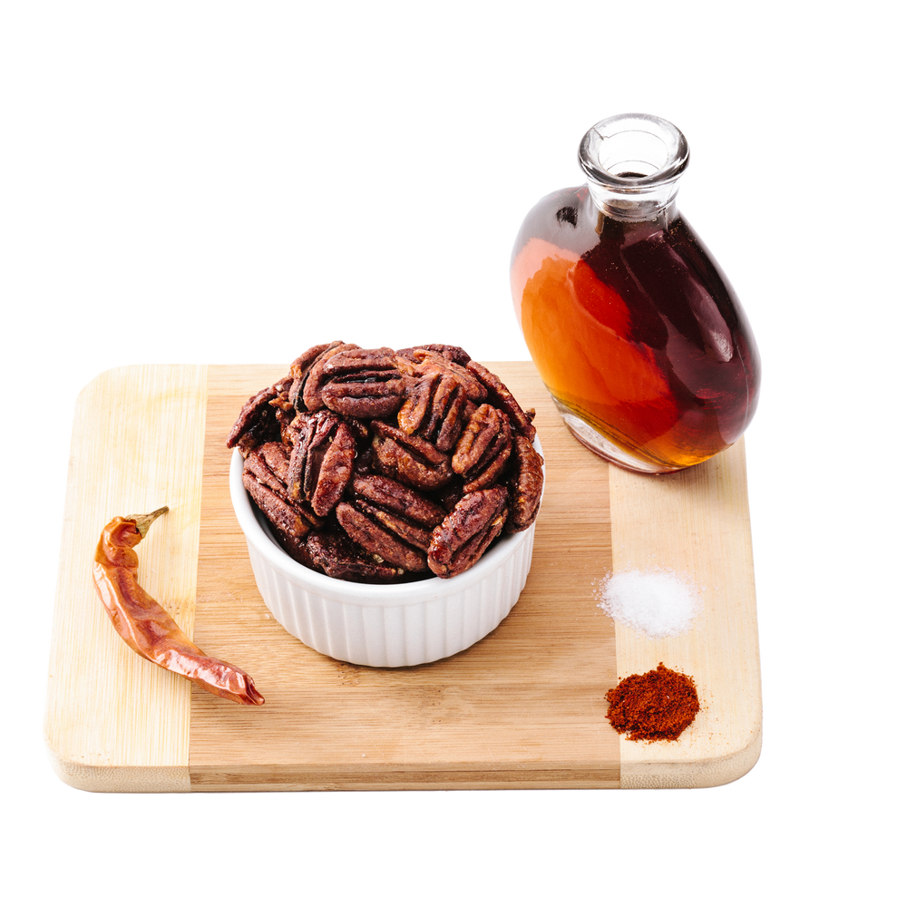Smoke maple pecans in white ramekin on wooden cutting board with glass of maple syrup and spices