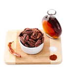 Smoke maple pecans in white ramekin on wooden cutting board with glass of maple syrup and spices